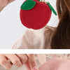 A close-up of a red fruit series coin purse keychain with green leaves, being held by a person.