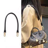 A close-up of a brown cowhide leather shoulder bag with a black strap and gold hardware.