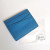 Porte-cartes en cuir véritable bleu texturé dans une pochette en plastique transparent.
