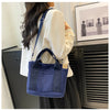 A woman holds a navy blue canvas crossbody bag with an adjustable strap and multiple pockets against a dark background.