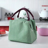 A green and white striped thermal lunch bag with a dark purple handle sitting on a white countertop.