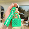 A hand holds a green silicone heart beach bag keychain with a gold split ring.