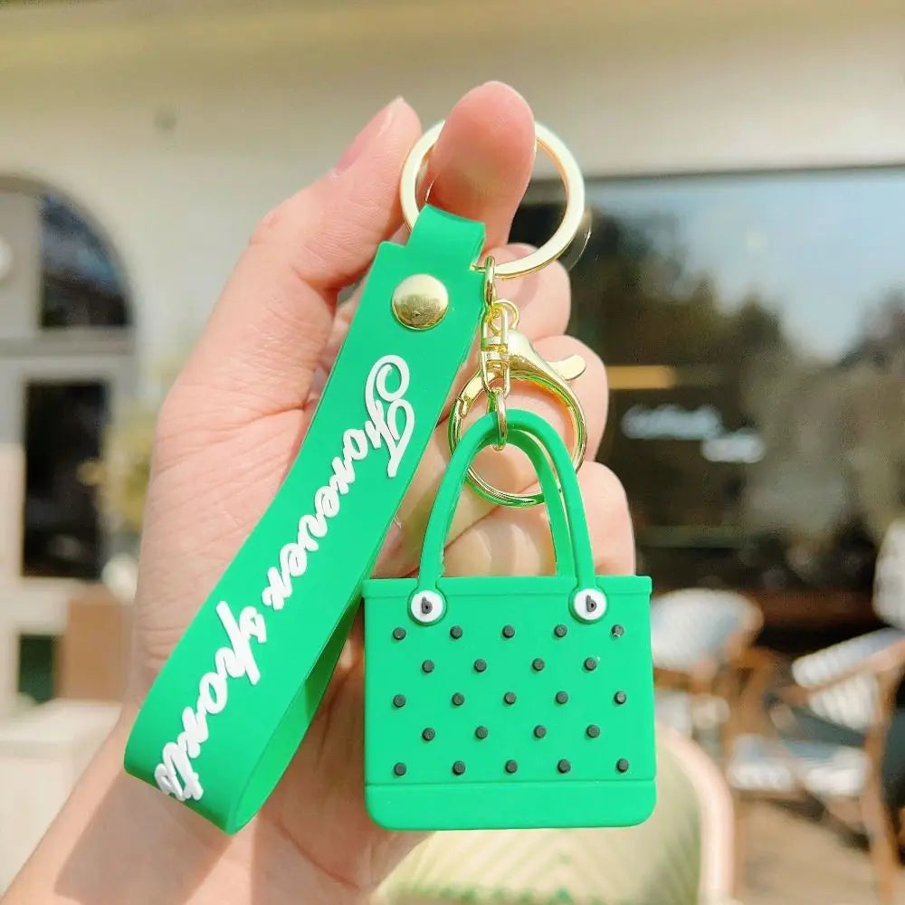 A hand holds a green silicone heart beach bag keychain with a gold split ring.