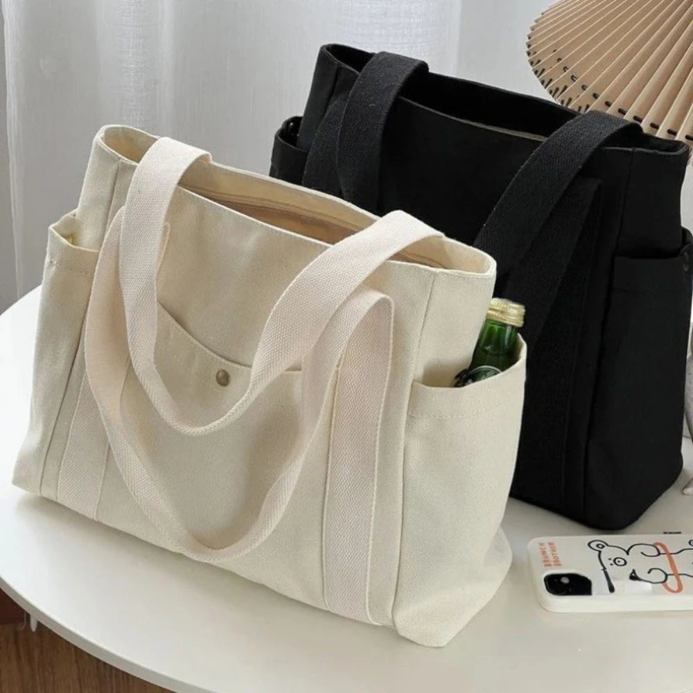 Una bolsa de lona beige junto a una bolsa negra, con una pequeña botella verde dentro.