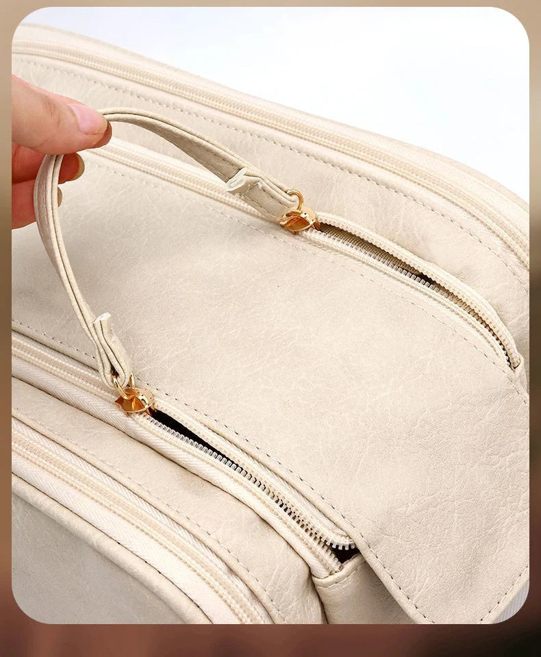 A hand is opening a beige PU leather travel makeup organizer featuring double zippers.