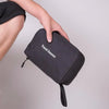 Une main tient un sac de toilette imperméable noir suspendu avec l'inscription Travel Season.