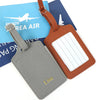 A set of two custom PU leather luggage tags, one gray and one brown, featuring a cross-pattern detail.