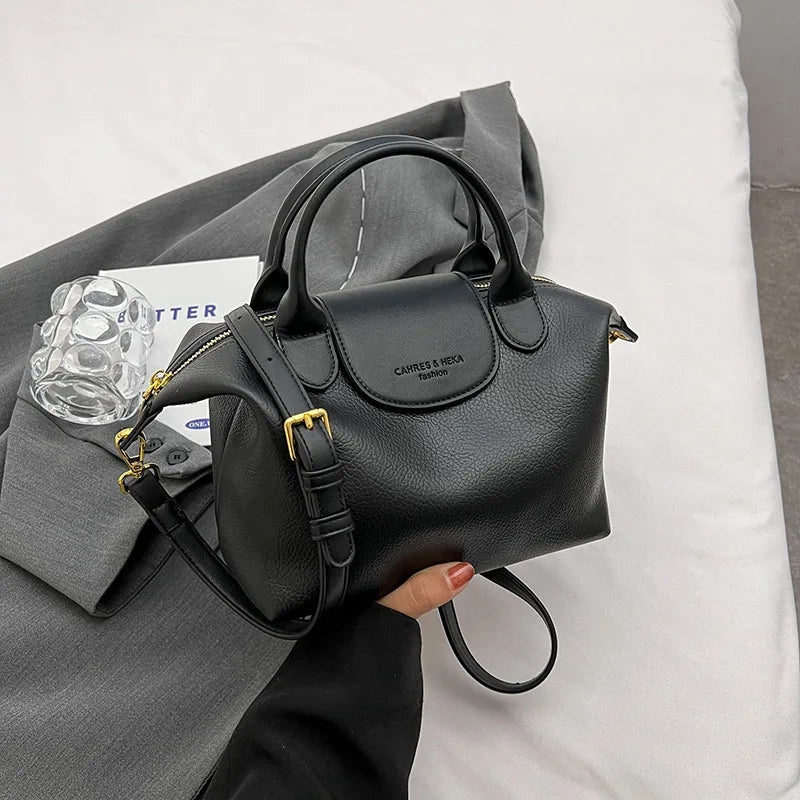 A black vintage PU leather crossbody handbag with gold hardware resting on a white surface.