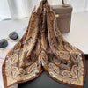 A brown and gold paisley silk hair scarf draped on a white surface.