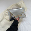 Silver crocodile pattern coin purse clutch held by a hand against a cream blazer.