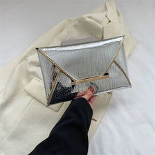 Silver crocodile pattern coin purse clutch held by a hand against a cream blazer.