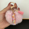 A hand holds a custom initial letter keychain featuring a shiny resin pendant and pink alphabet charm attached to a fluffy pi