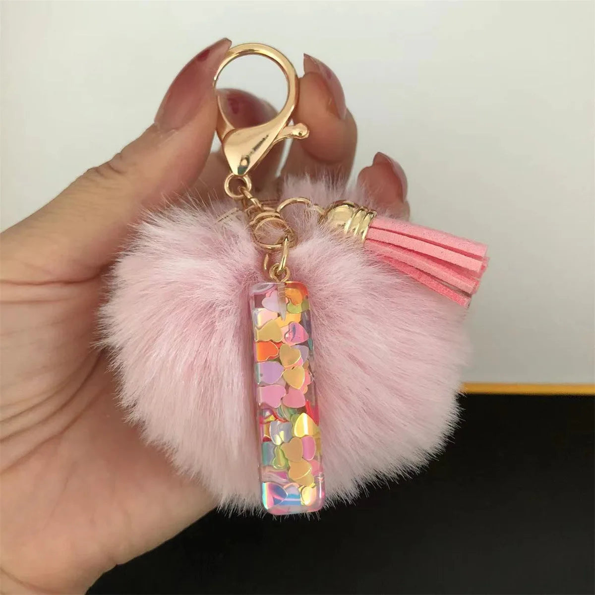 A hand holds a custom initial letter keychain featuring a shiny resin pendant and pink alphabet charm attached to a fluffy pi