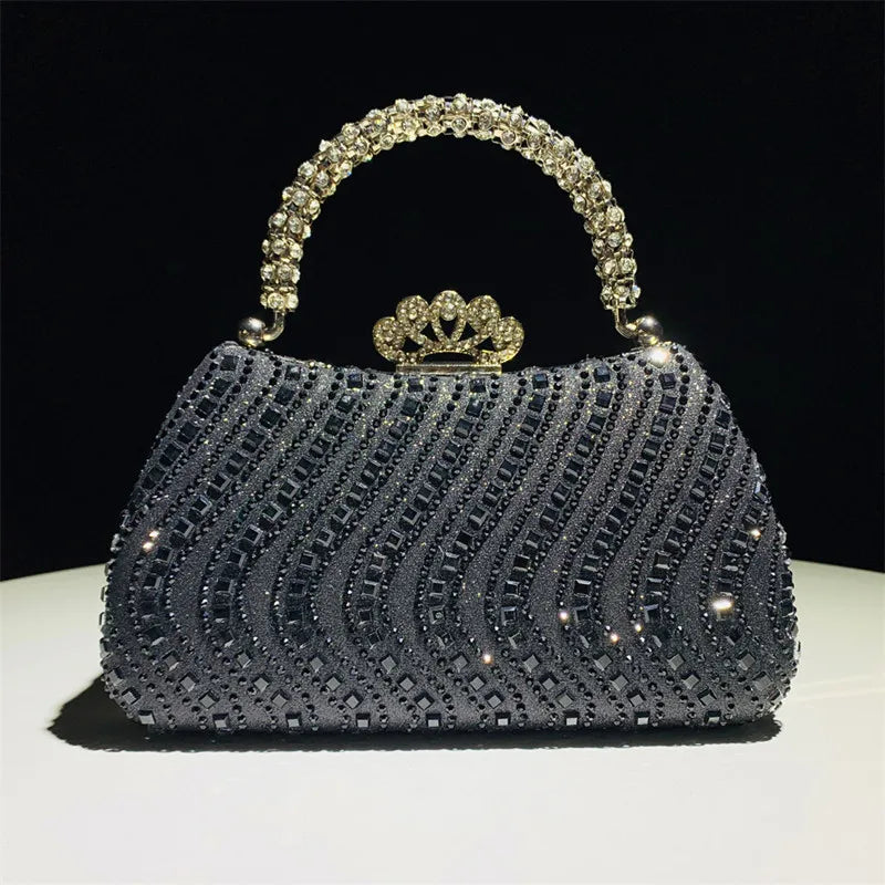 A dark gray crystal-embellished evening clutch bag with a gold crown clasp and chain strap.