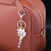A gold-toned rhinestone bow and heart key chain charm attached to a brown leather handbag.