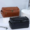 A brown leather toiletry bag next to a black leather version on a white surface.
