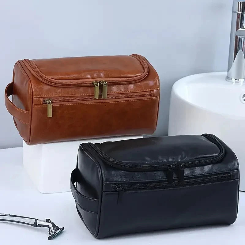 A brown leather toiletry bag next to a black leather version on a white surface.