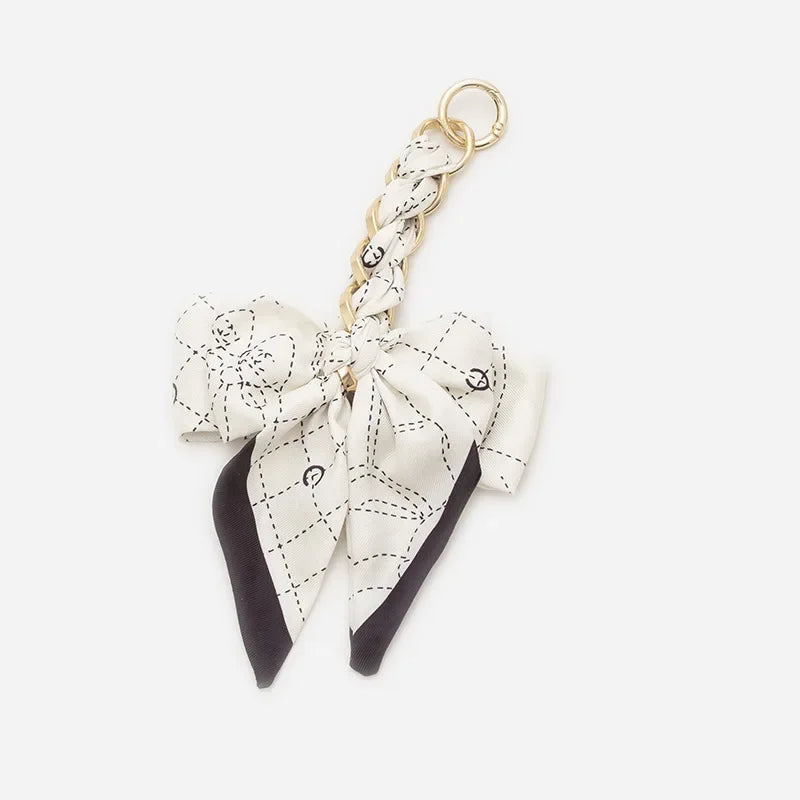 A white and black patterned bow bag chain strap extension with a gold ring.