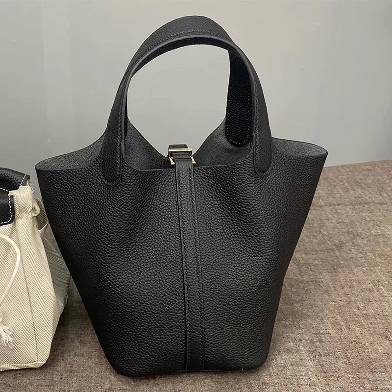 A black classic genuine leather bucket bag is shown standing upright on a brown surface.
