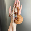 A hand holds a leather croissant keychain with a lanyard and pendant.