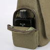 A dark glass bottle labeled BLUE DE is stored inside a olive green canvas messenger bag.