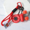 Red fitness dumbbell keychain charm with a black strap and chain attached to a white rock.