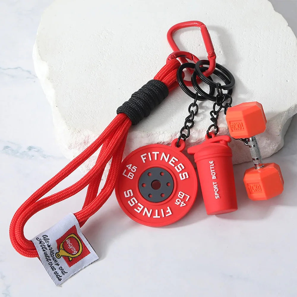 Red fitness dumbbell keychain charm with a black strap and chain attached to a white rock.
