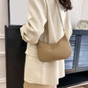A beige PU leather shoulder bag with a thin strap is held by a person wearing a light colored blazer.