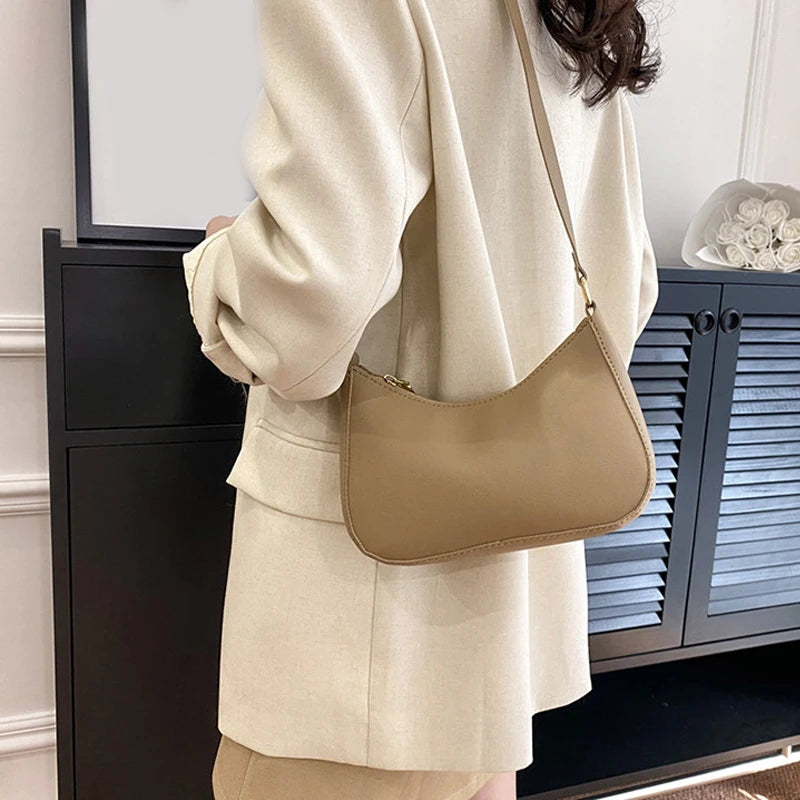 A beige PU leather shoulder bag with a thin strap is held by a person wearing a light colored blazer.