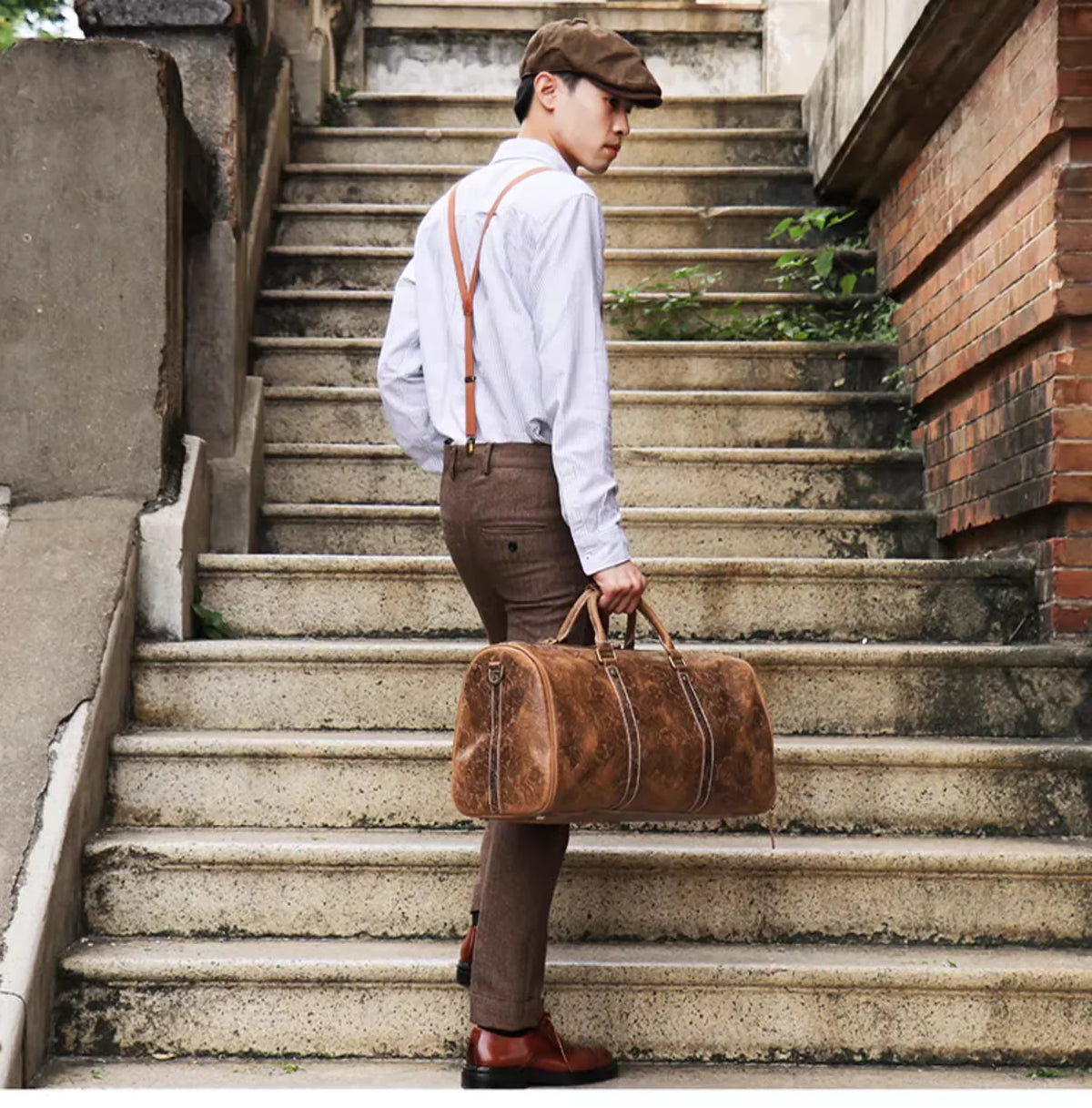 Mann in weißem Hemd und braunen Hosen steht auf Steinstufen und trägt eine vintage geprägte Leder-Tasche.