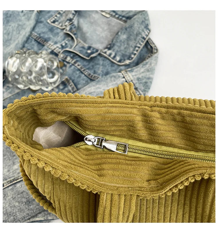 A close-up of a mustard yellow corduroy handbag with a silver zipper, set against a denim background.