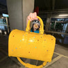 A person is holding a bright yellow faux crocodile tote bag with crystal accents in an indoor setting.