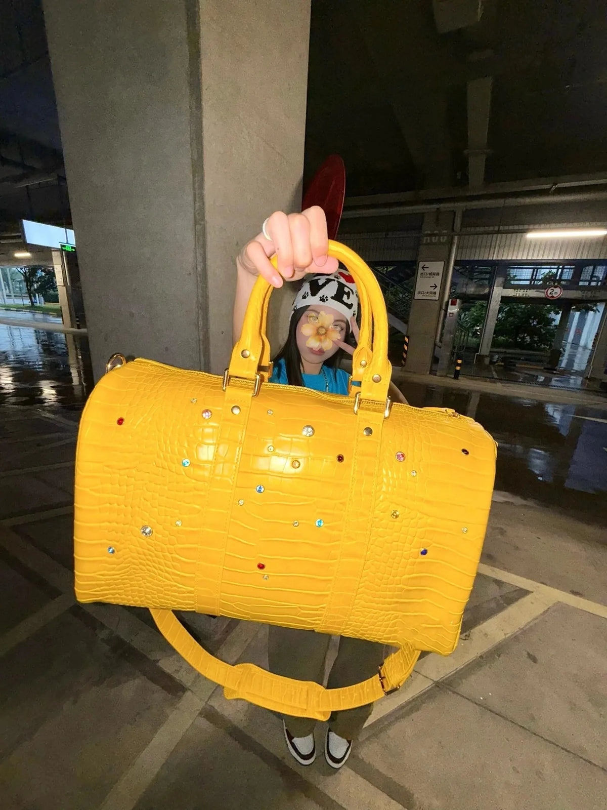 A person is holding a bright yellow faux crocodile tote bag with crystal accents in an indoor setting.