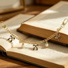 A gold chain necklace with butterfly and bow charms rests on an open book.