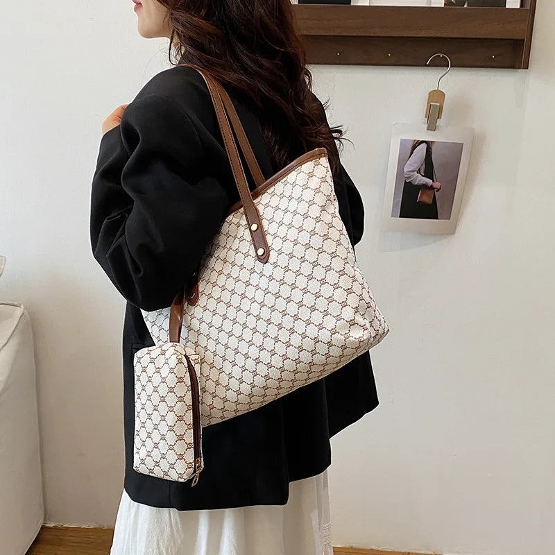 A woman holds a beige geometric patterned tote bag with brown leather trim against a white wall.