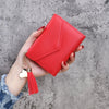 A hand holds a red PU leather coin clutch wallet with a gold tassel against a gray background.