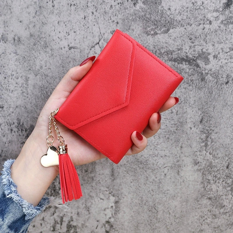 A hand holds a red PU leather coin clutch wallet with a gold tassel against a gray background.