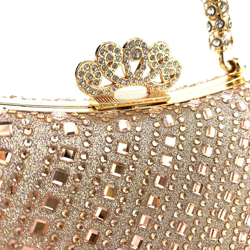 A close-up of a crystal-embellished gold clutch bag with a crown clasp and a gold chain strap.