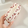 A hand holds a quilted storage pouch with a red cherry and bow print on a light cream fabric.