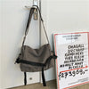 Bolso cruz de lona en cuero gris colgado en una puerta blanca.