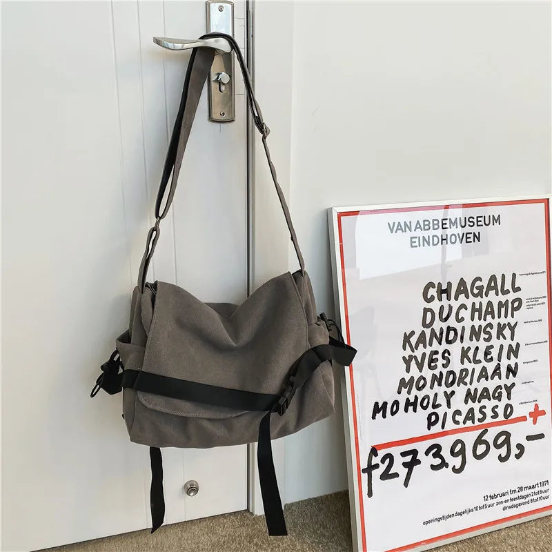 Bolso cruz de lona en cuero gris colgado en una puerta blanca.