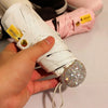 A hand holds a white compact umbrella with gold accents and a rhinestone sphere attached.