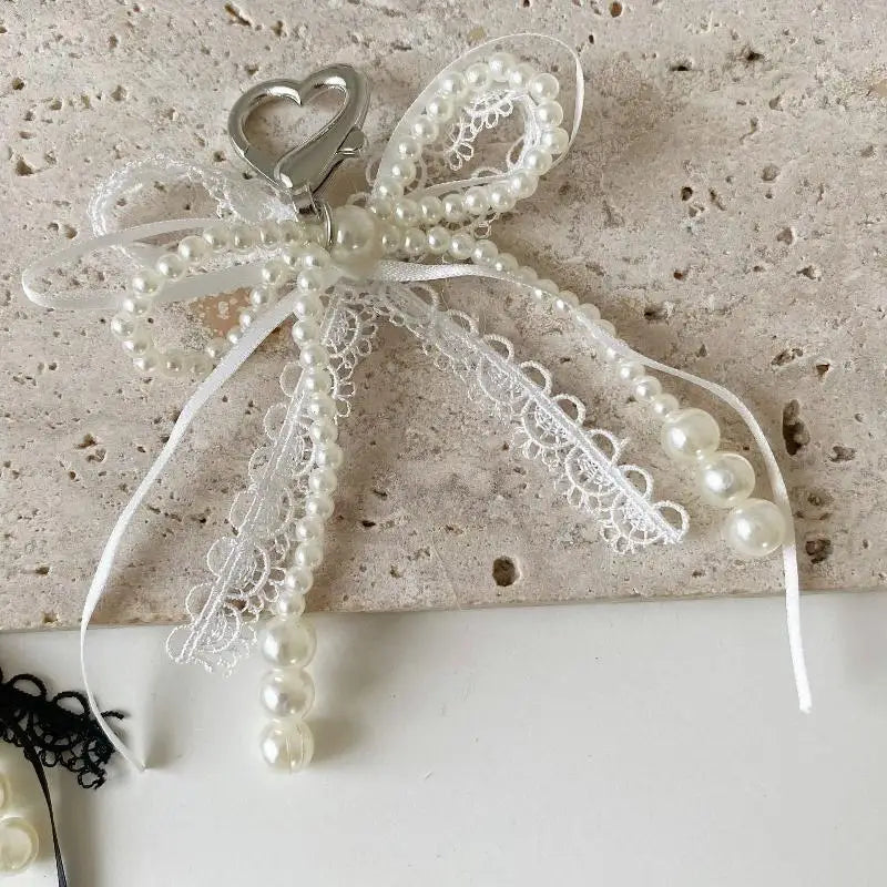 A white pearl bowknot keychain featuring delicate lace and a heart charm.