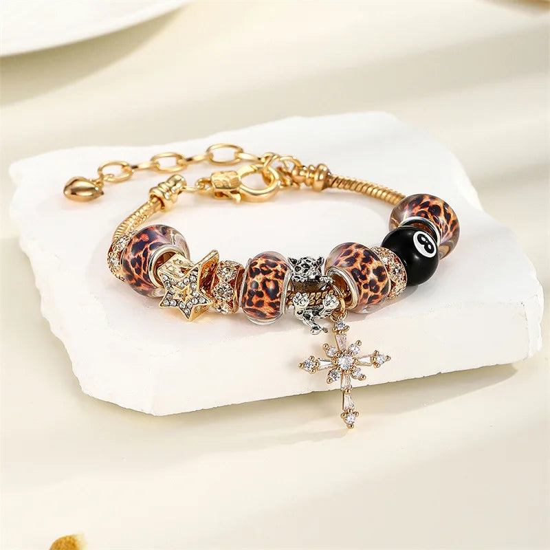 A gold-toned bracelet featuring leopard print and black beads with a star charm and a cross pendant.