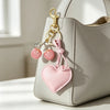 A light gray leather handbag with a pink cherry heart keychain attached to the zipper pull.