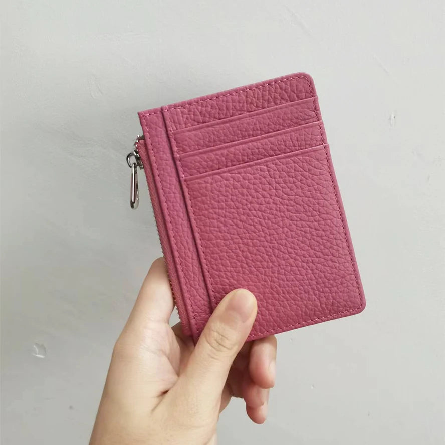 A hand holds a pink genuine leather zipper card holder and coin purse.
