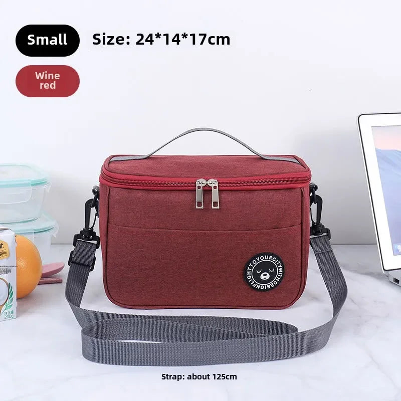 A maroon insulated portable lunch bag with a gray shoulder strap is shown on a white surface.