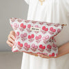 A pink floral canvas makeup bag with a butterfly pattern is held by a person against a white dress.