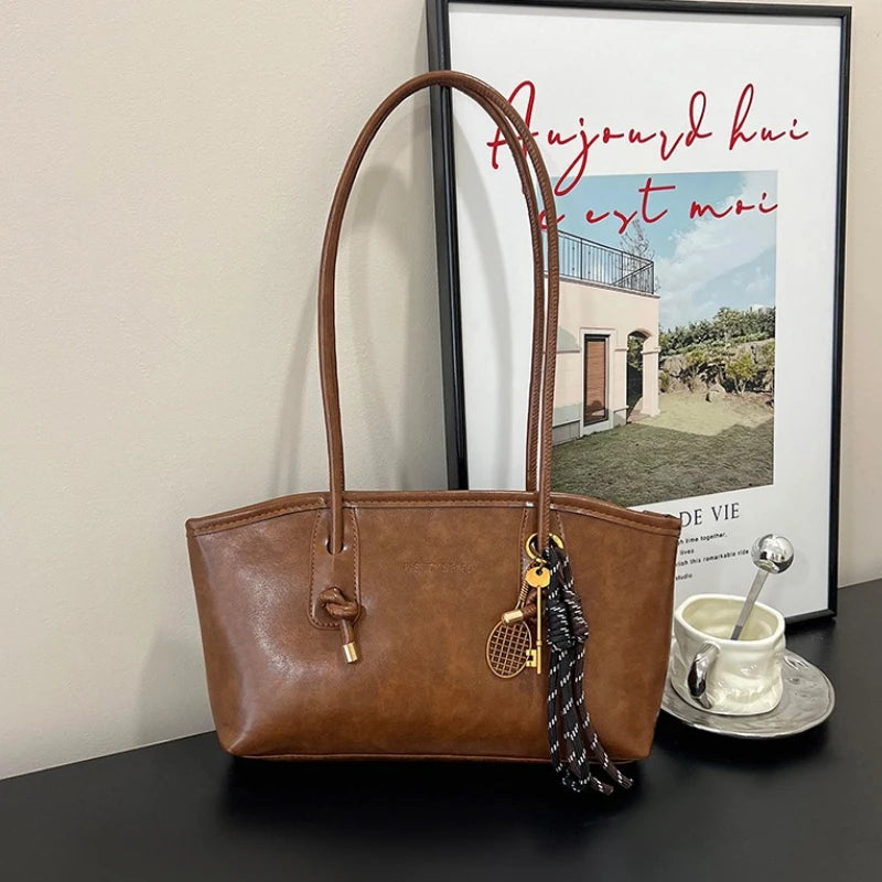 A brown classic PU leather tote bag hanging against a white wall with a framed print.