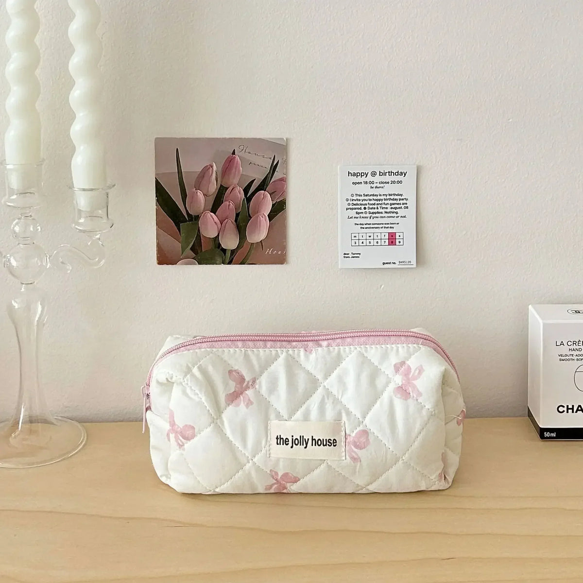 Sac de rangement cosmétique en matelassé blanc avec imprimés de nœud rose posé sur une surface en bois à côté d'une carte d'a